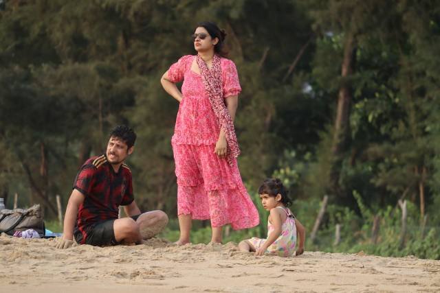 A family laughing together on the beach, swinging their son between them